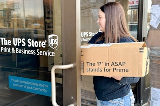 a woman walking into a UPS store with an amazon package to return