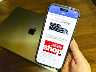 a hand holding a cell phone with costco trade in program on screen 