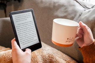 a person holding a kindle and a cup of coffee
