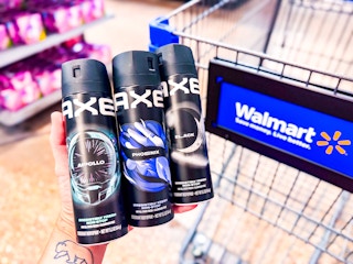 hand holding three bottles of axe body sprays in front of walmart cart in aisle