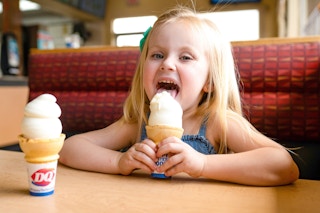 Little girl licking and ice cream cone sitting at a booth in Dairy Queen